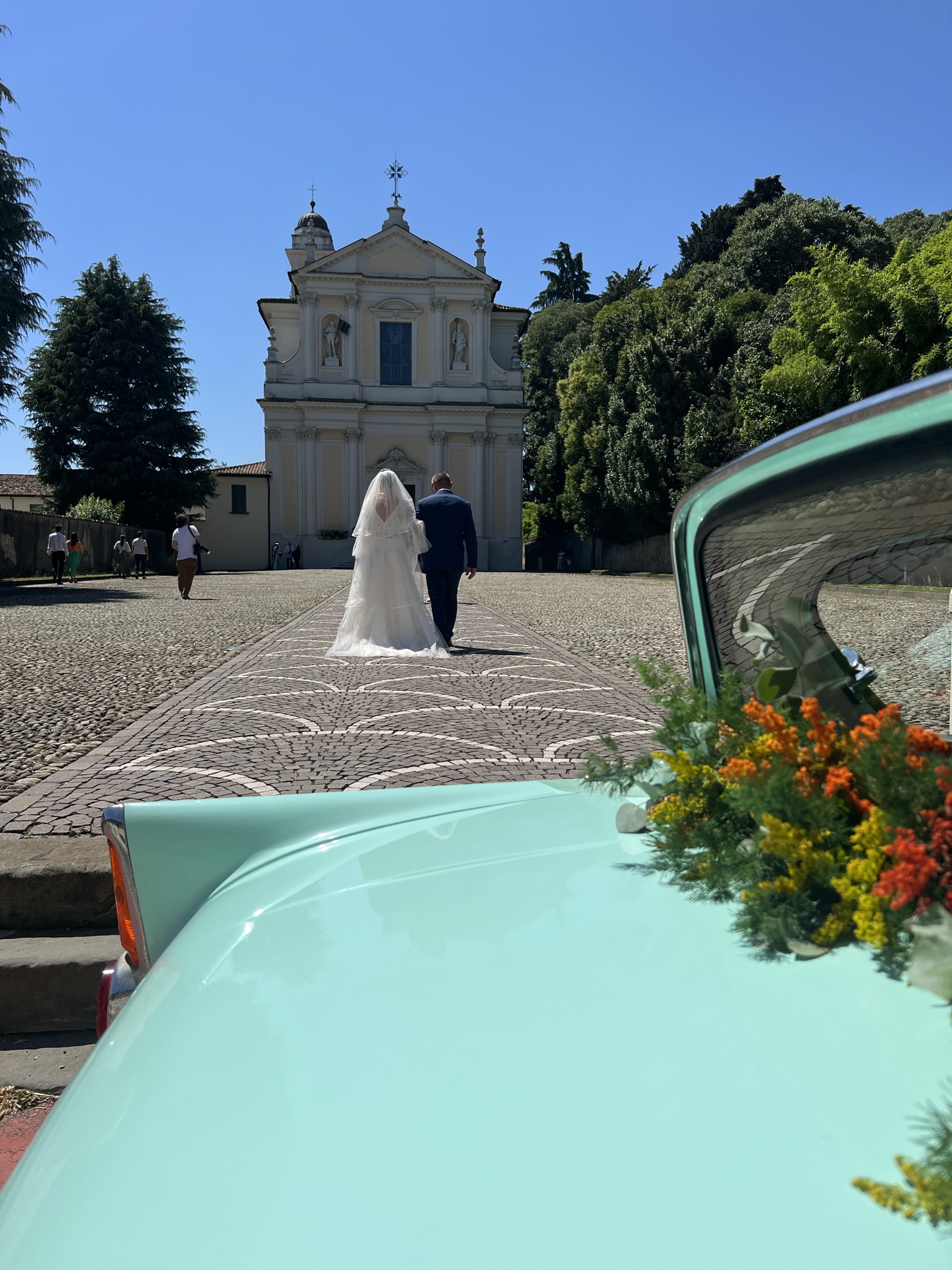 Sposi verso la chiesa con la Ford Anglia azzurra in primo piano